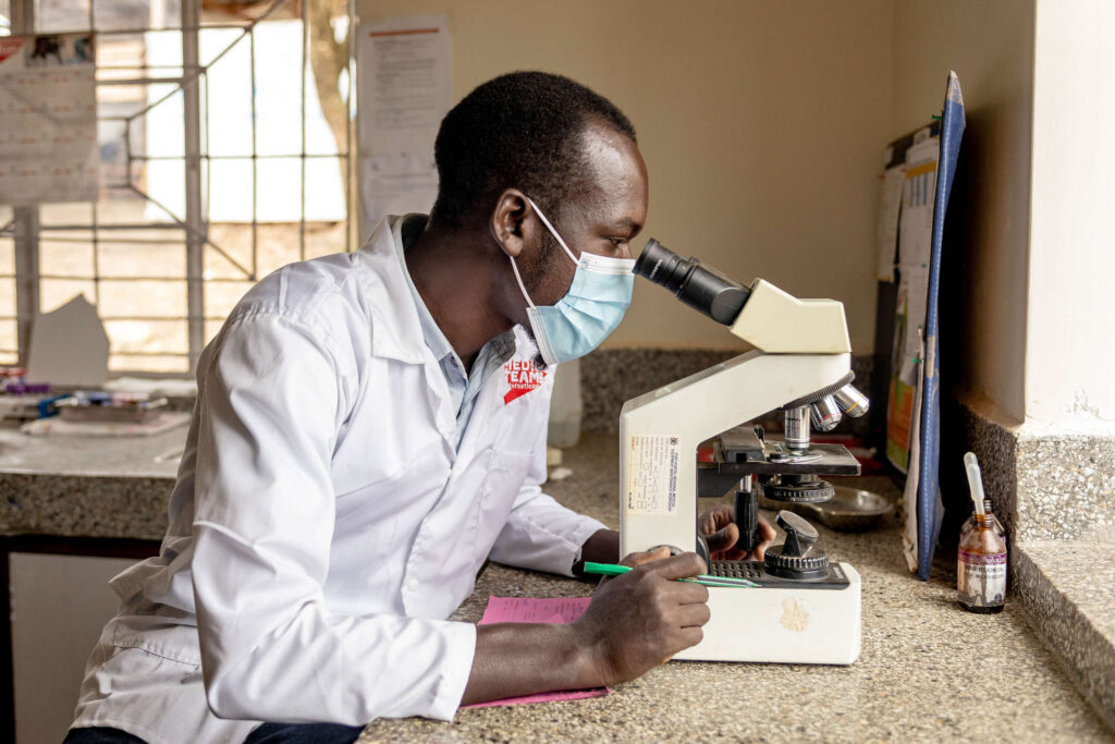 A health worker looks into a microscope in a lab.