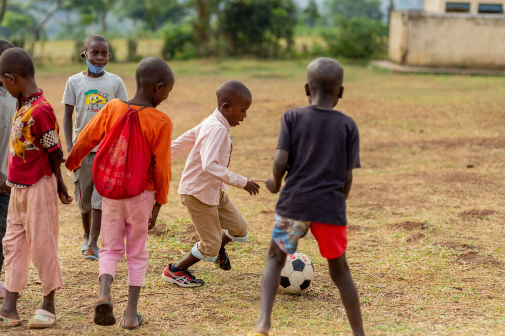 Thiery plays soccer with several kids in a field.